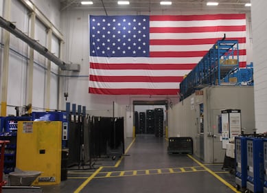 A large United States flag hangs from a wall inside a large warehouse.